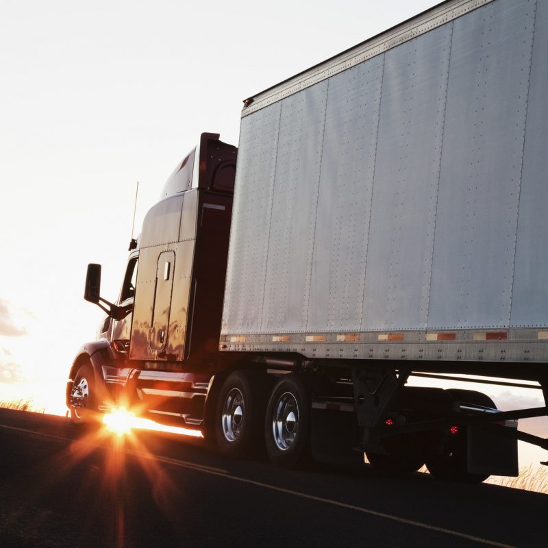 Silhouette of a commercial truck driving on a highway at sunset.